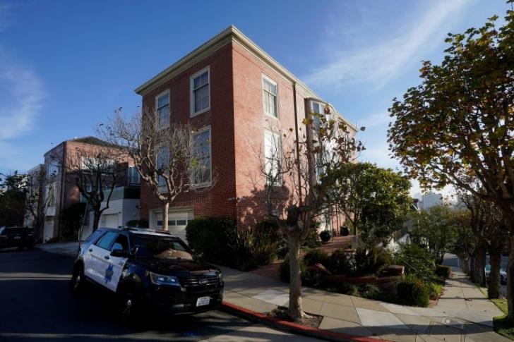 A police car parked on an inclining street in front of a tall brown brick house. 